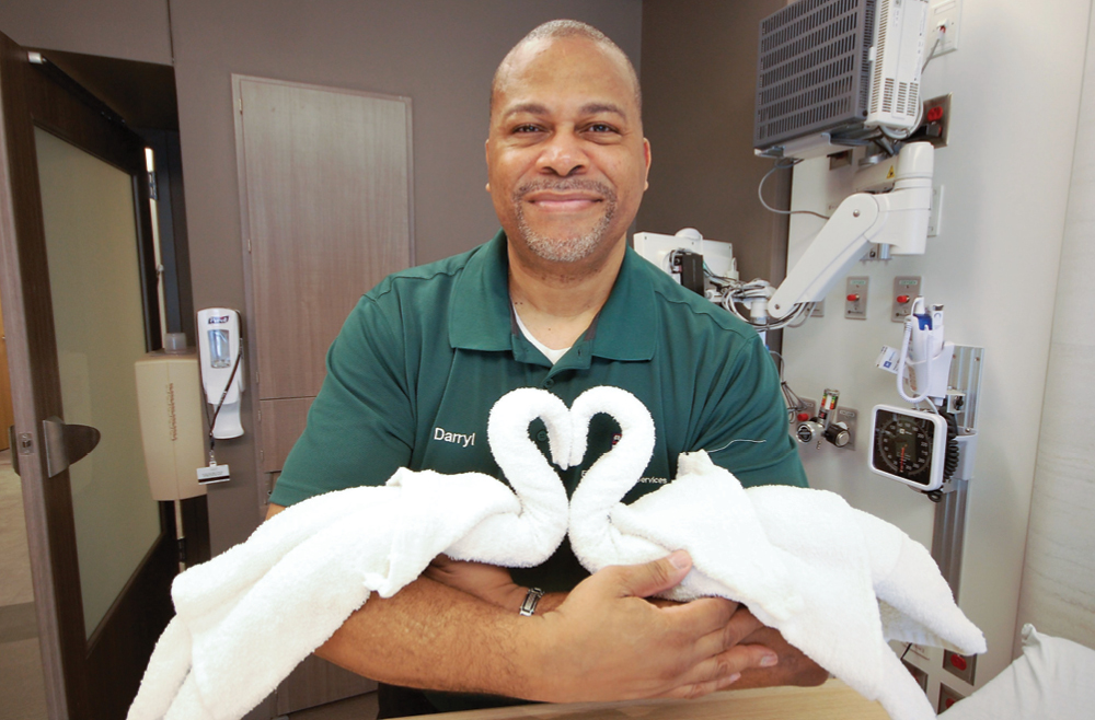 Environmental Services attendant Darryl Simms with two towels folded into the shape of swans facing each other. 